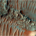 Kleurenfoto van de sterk geërodeerde stroomruggen in Noachis Terra op Mars. Her en der worden de ruggen doorkruist door zandduinen. © HiRISE Image: ESP_085386_1505 NASA/JPL/University of Arizona