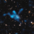 Artist’s impression van de protocluster rond het Spinnenwebstelsel. De meeste massa bevindt zich niet in de sterrenstelsels in het centrum, maar bestaat uit heet gas (‘blauwe wolk’). © ESO/Di Mascolo et al.; HST: H. Ford