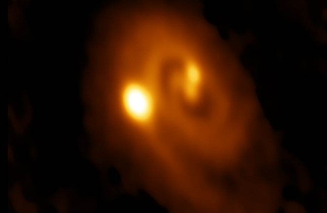 ALMA-opname op een golflengte van 1,3 mm van de drievoudige protoster L1448 IRS3B. De opname laat de spiraalstructuur en de emissie naar de drie protosterren zien. De helderste emissie is richting het buitenste en jongste lid van het trio.  De opname besl