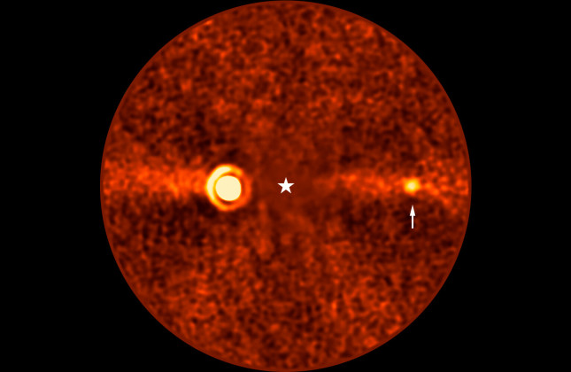 De ontdekte planeet Bèta Pictoris d (bij de witte pijl) op een opname van de Very Large Telescope. Het licht Bèta Pictoris is geblokkeerd (de witte ster). Links is de planeet Bèta Pictoris b zichtbaar. (c) ESO/B. Sutlieff, M. Bonse et al.