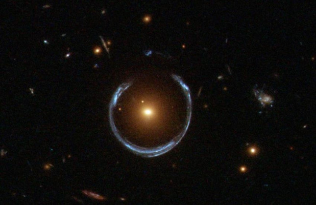De zwaartekrachtlens die het Kosmische Hoefijzer wordt genoemd. Het pas ontdekte ultra-zware zwarte gat bevindt zich in het centrum van het oranje sterrenstelsel. © NASA/ESA