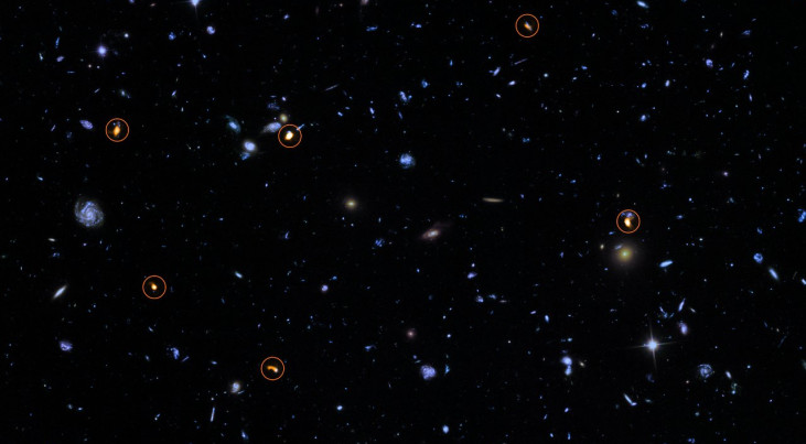 Deze foto is een combinatie van een achtergrondfoto, gemaakt door Hubble van NASA en ESA (blauw/groen) en een nieuwe, zeer diepe ALMA-opname van hetzelfde gebied (oranje en omcirkeld). Alle objecten die ALMA ziet blijken zware, sterren-vormende sterrenste