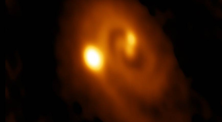 ALMA-opname op een golflengte van 1,3 mm van de drievoudige protoster L1448 IRS3B. De opname laat de spiraalstructuur en de emissie naar de drie protosterren zien. De helderste emissie is richting het buitenste en jongste lid van het trio.  De opname besl